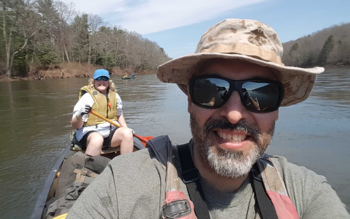 two people smile at the camera while paddling a canoe on an outward bound course